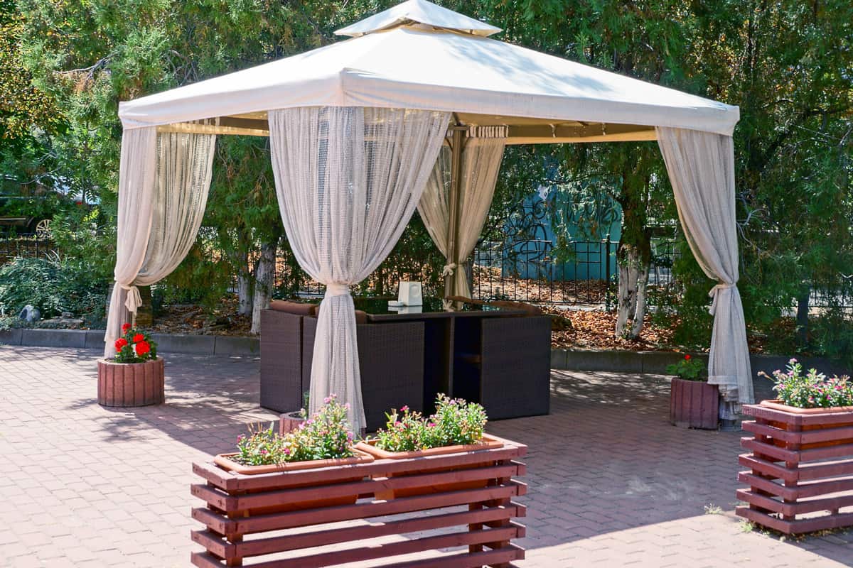 Outdoor gazebo with curtains and furniture on the sidewalk in the park.