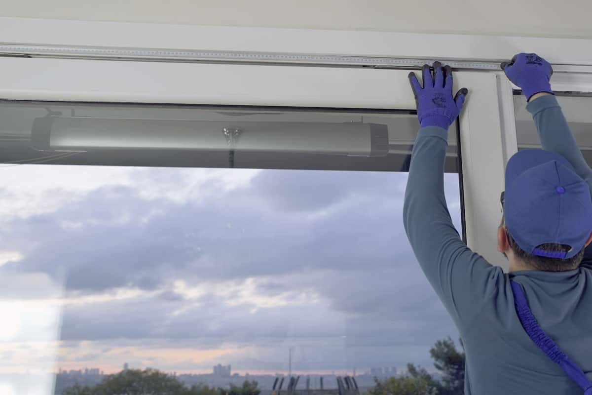 photo of a man wearing blue clothings installing window on the house