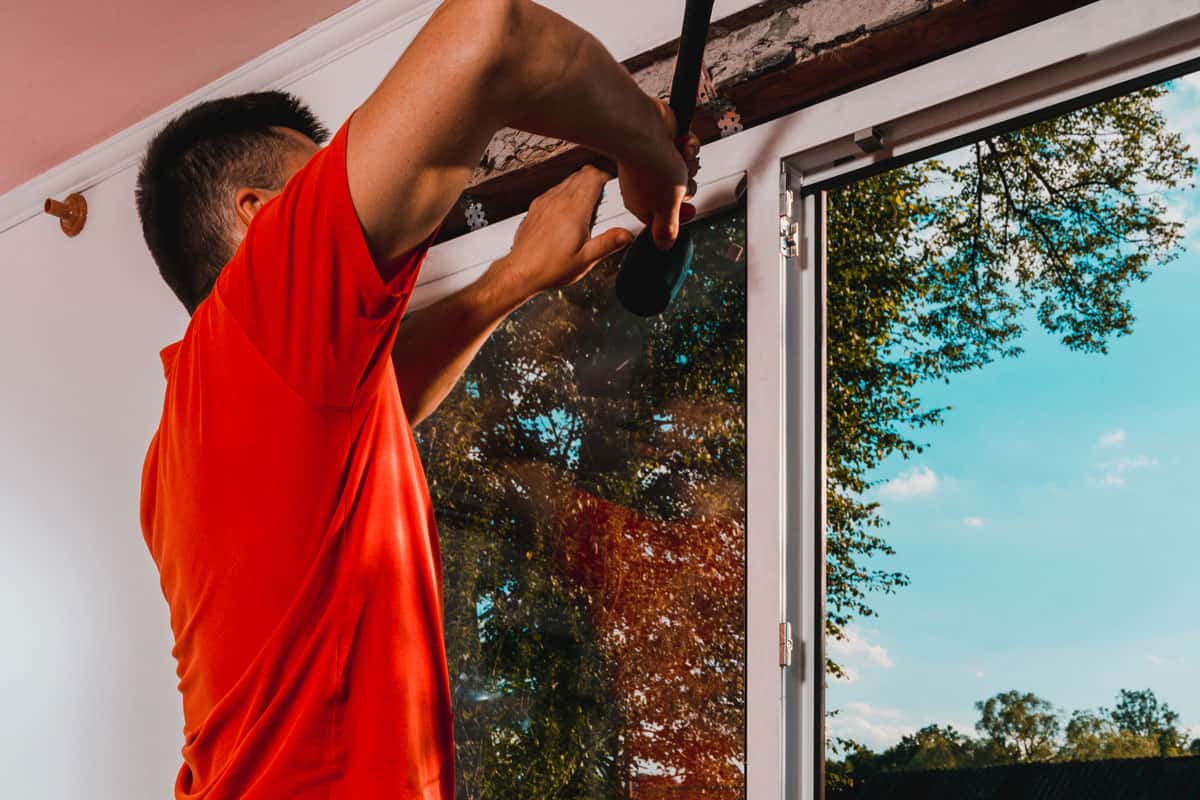 photo of a man wearing red shirt fixing house wall window on the wall of bed room