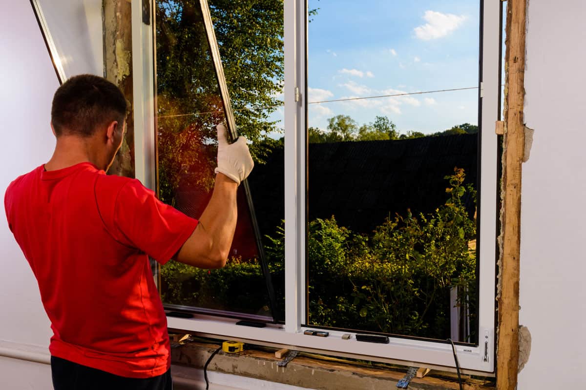 photo of a red shirt man installing window on the wall of the house