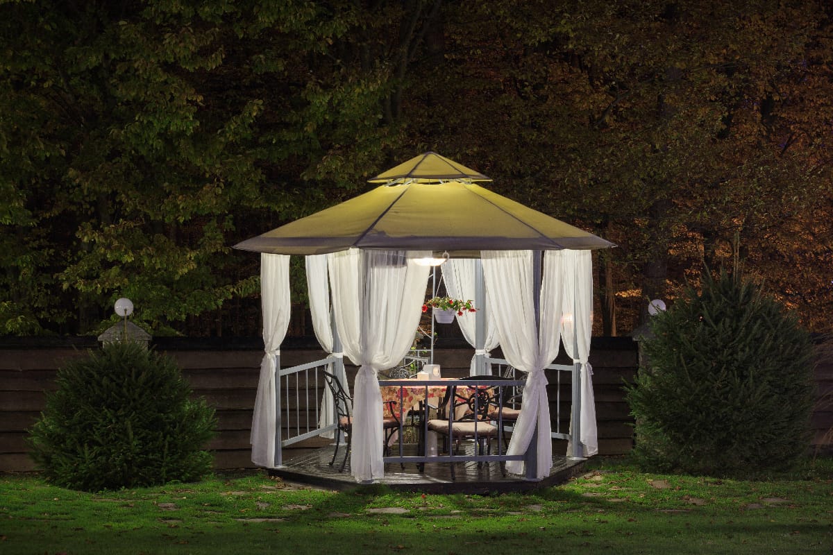 A beautiful gazebo with a table in the evening, autumn park is lit by a lamp