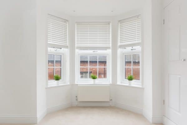 An empty modern room in an urban apartment with plain white walls and bay window, Should Bay Windows Have Shutters?