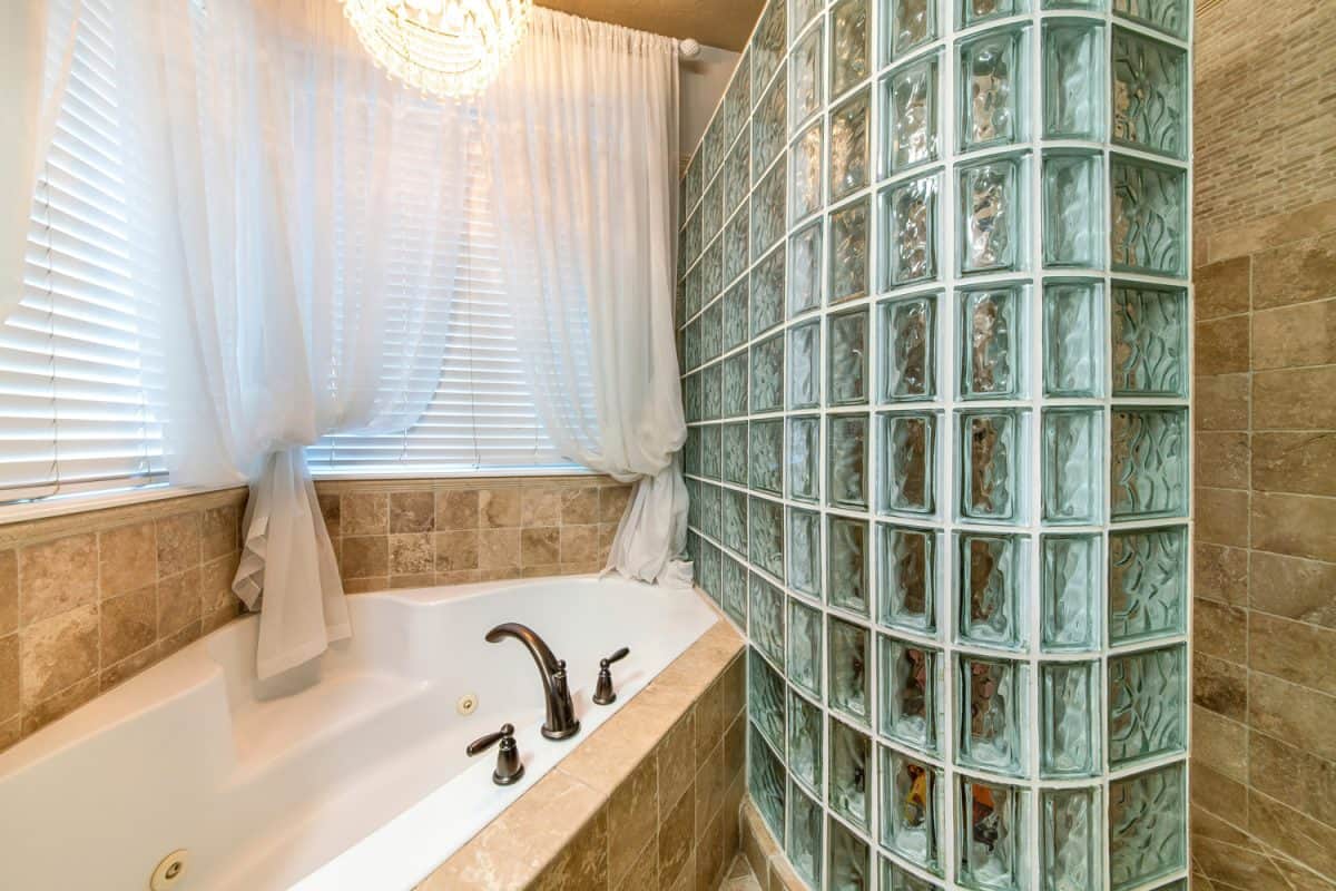 Bathroom interior with corner bathtub and stall with glass block wall
