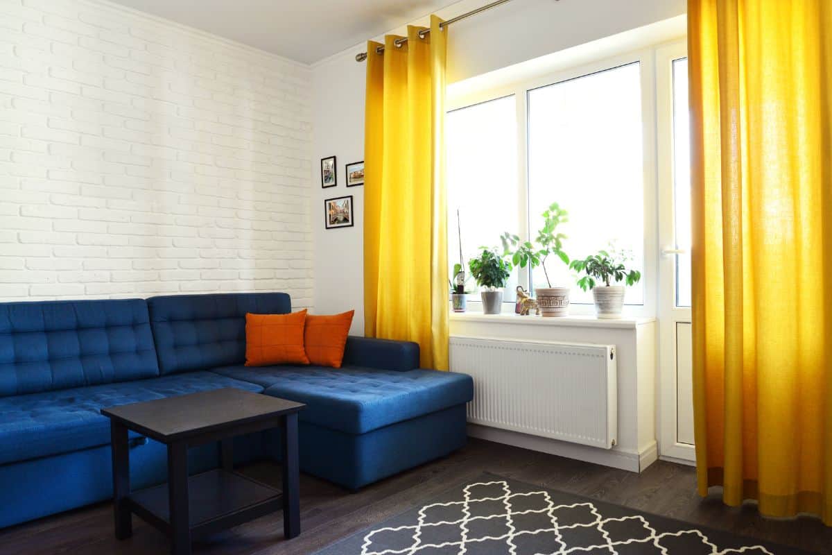 Clean family room with blue couch, white brick wall and yellow curtains. Design interior concept.
