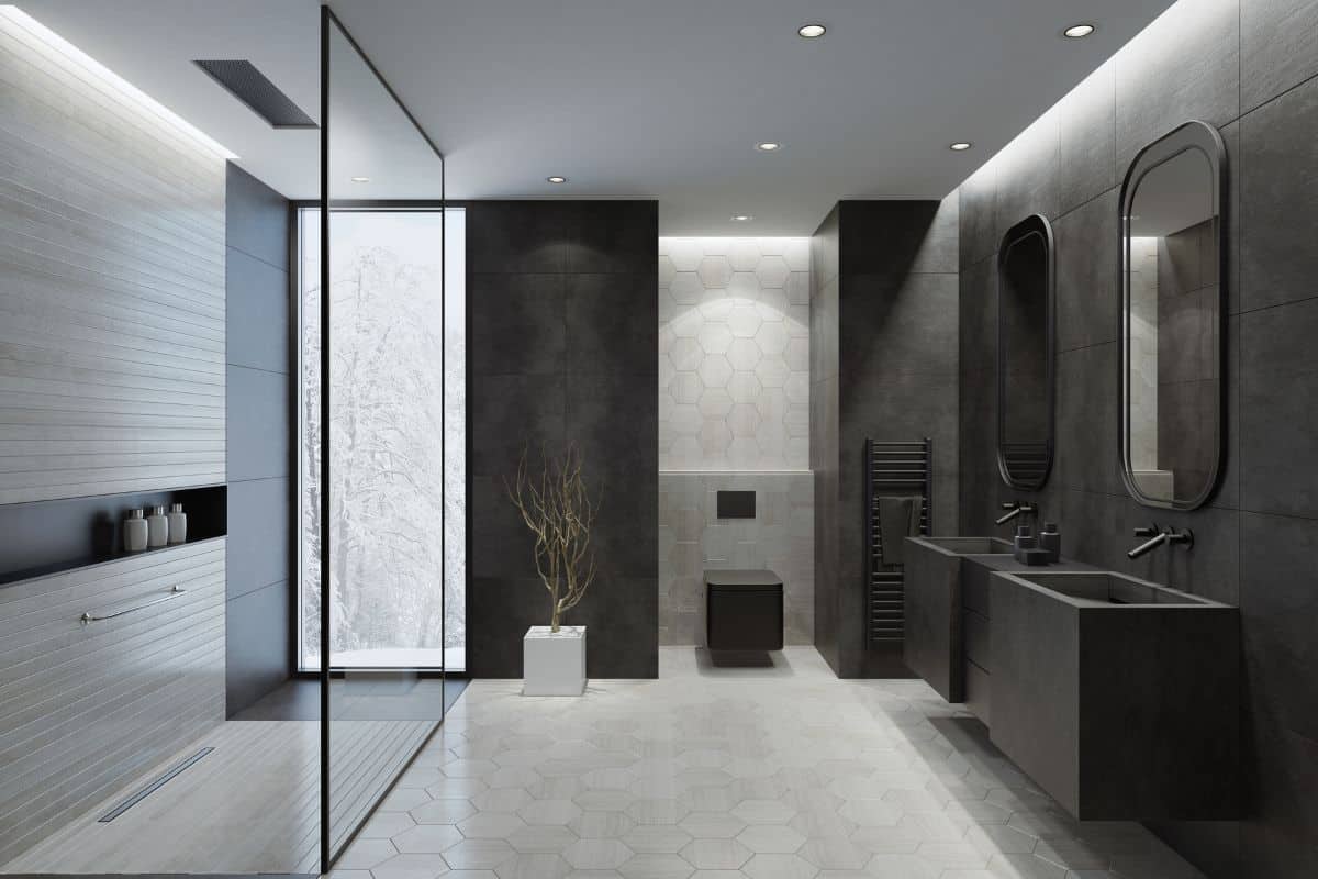 Contemporary bathroom with light gray honeycomb ceramic tiles and dark gray concrete like large tiles. Walls with trendy concrete like light gray large ceramic tiles. Floor with dominating light gray honeycomb ceramic tiles. Two gray stone washbasins with two wall-mounted black stainless steel bathroom sink faucets, black storage cabinet with drawers between. Two rectangular wall mirrors with gray metal frames. Walk-in shower with light gray long narrow ceramic tiles, glass wall and luxury ceiling mounted shower head. Separated black rectangular toilet mounted to a wall with honeycomb wall ceramic tiles. Ceiling with strip cove lighting and embedded spotlights. **background is my istock image