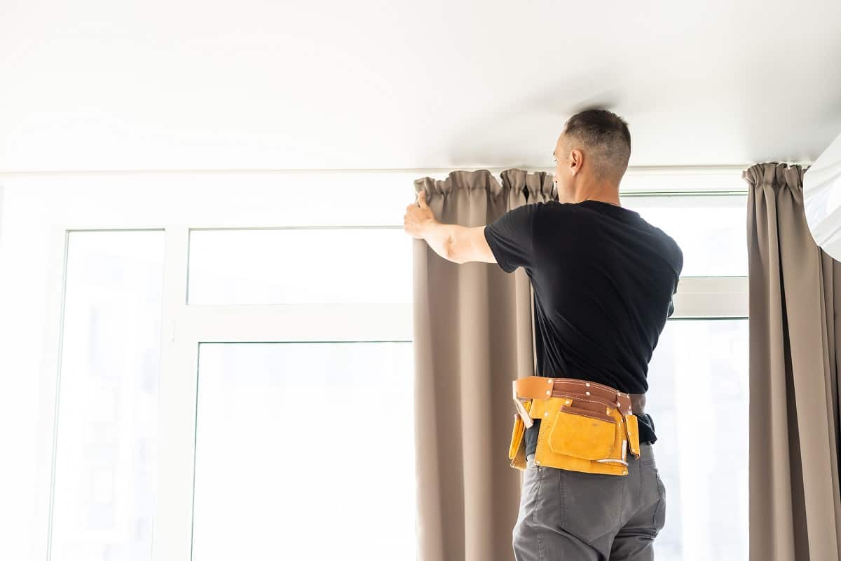 How To Install Curtains - worker repairman hanging and fixing the curtain on the window