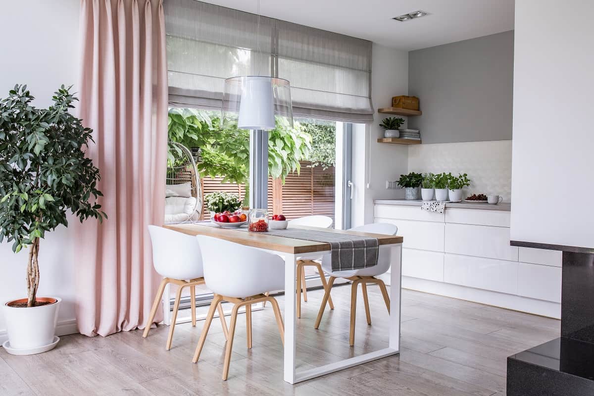 Incorporate Neutral-Toned Roman Shades - Gray roman shades and a pink curtain on big, glass windows in a modern kitchen