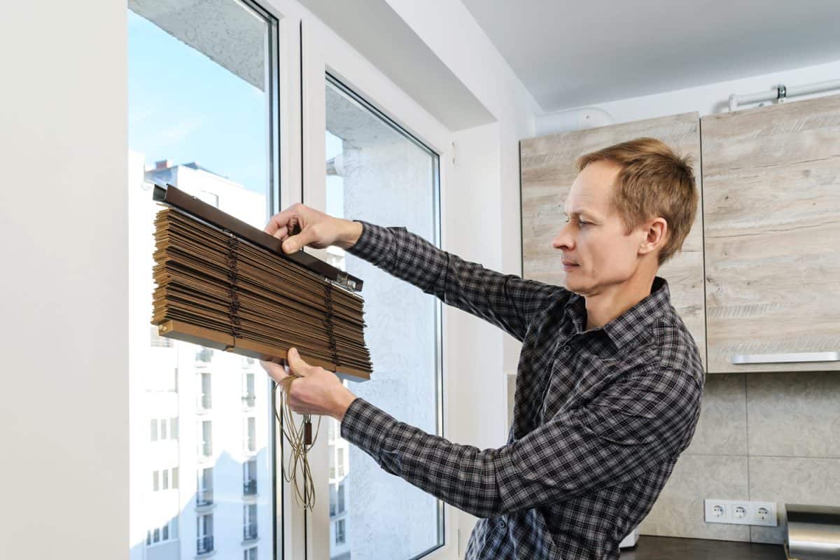 Installing wooden blinds. A man holds the folded jalousie.
