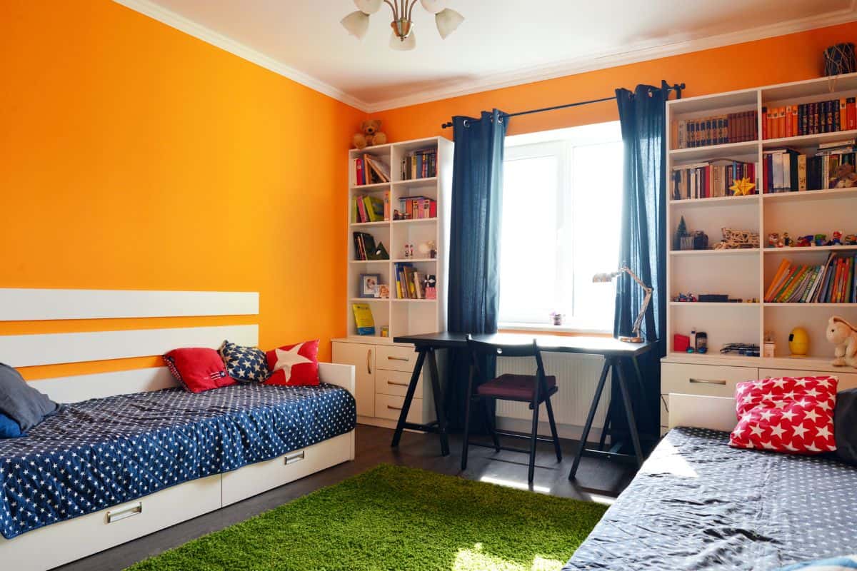 Kids bedroom in orange and blue colors with two beds and bookcases
