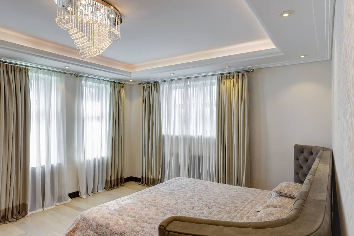 Modern and stylish interior of bedroom with crystal chandelier in center of ceiling