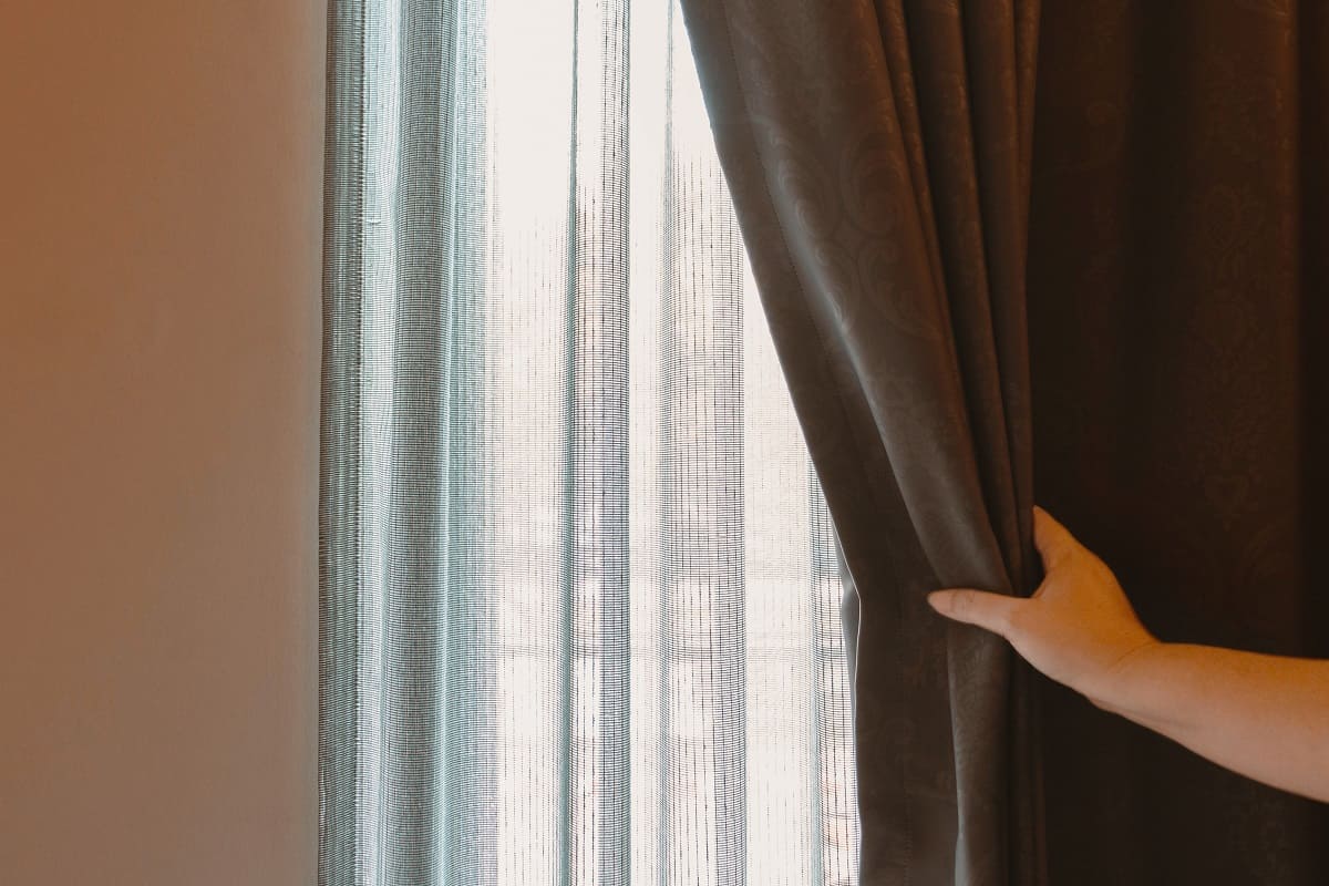 Pairing Curtains With Windows - woman's hand opening brown luxurous curtain over white translucent curtain