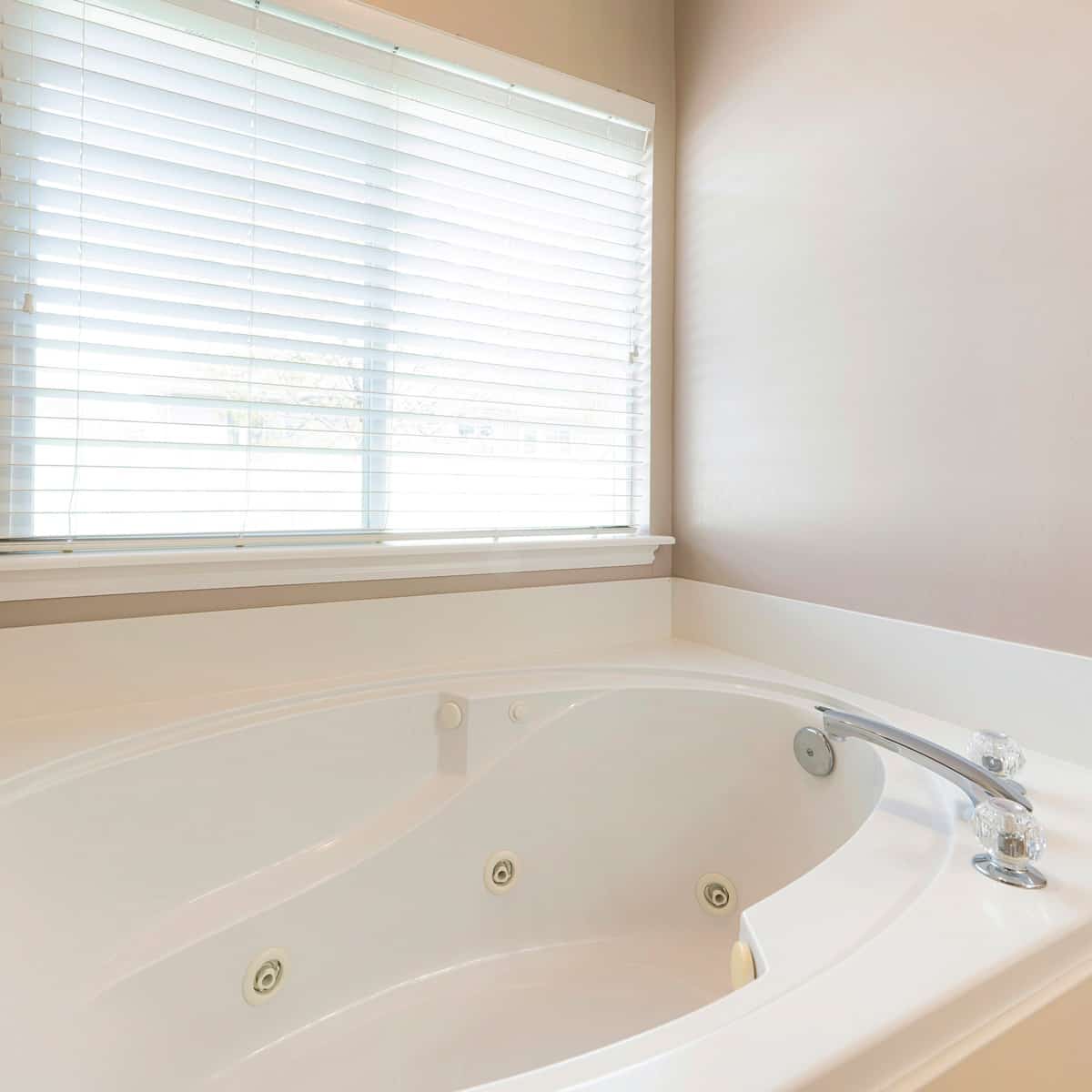 Square Drop-in bathtub in a bathroom with windows and blinds.