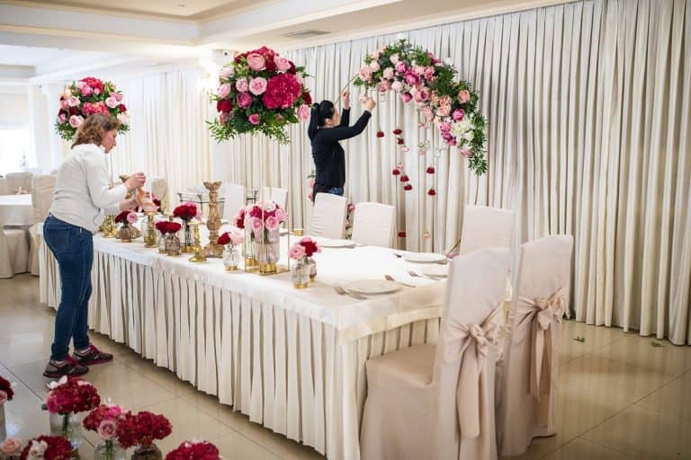 Two hard working women finishing decorating of banquet hall with blossom flowers, How To Hang Curtains In Garage For A Party?