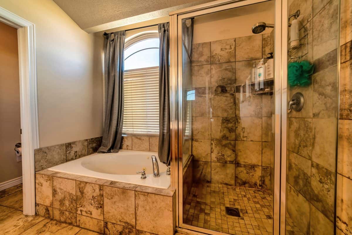 Warm toned bathroom with round bathtub tiles shower stall and arched window
