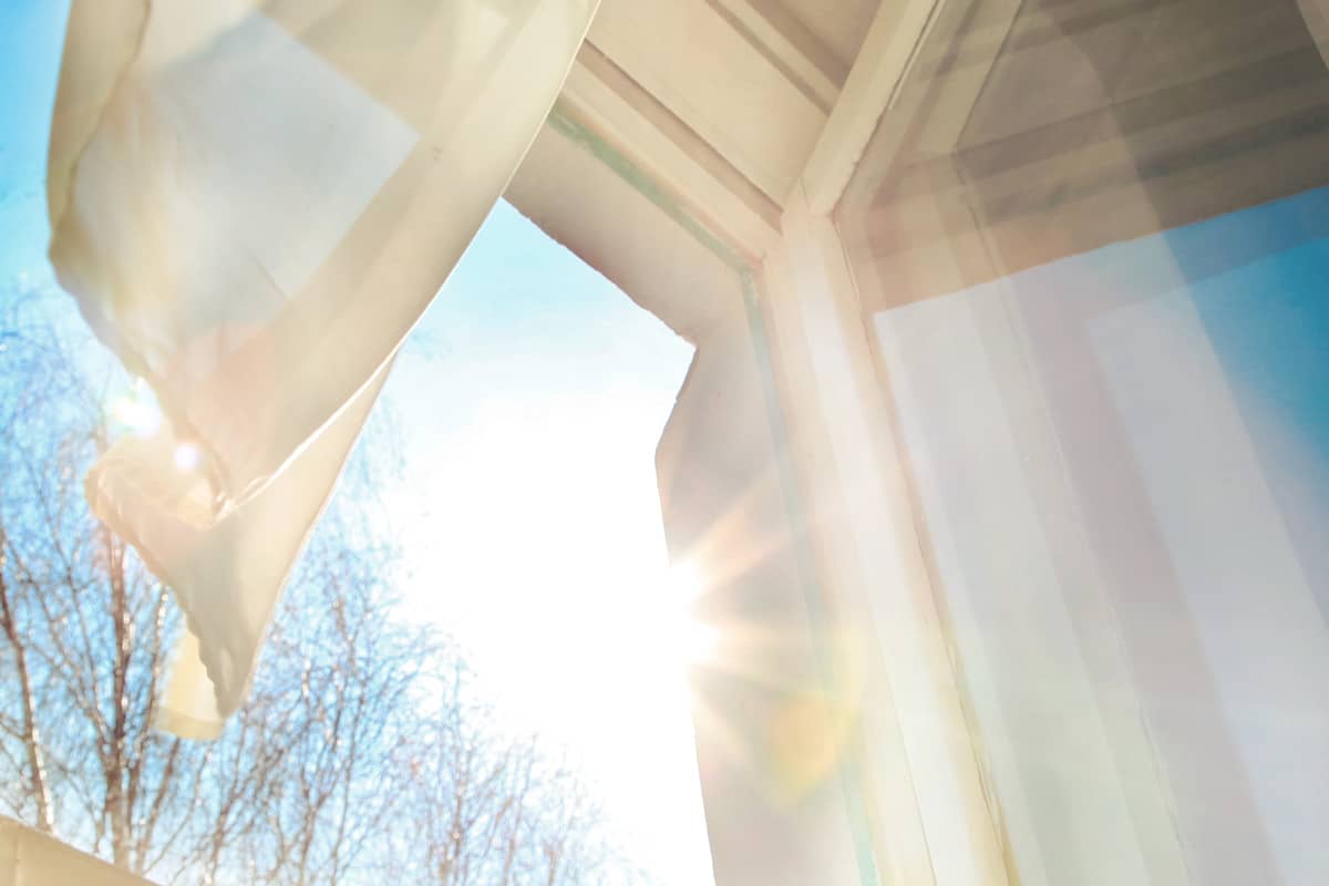 Window is open wind blows curtain sun shining through window blue sky background

