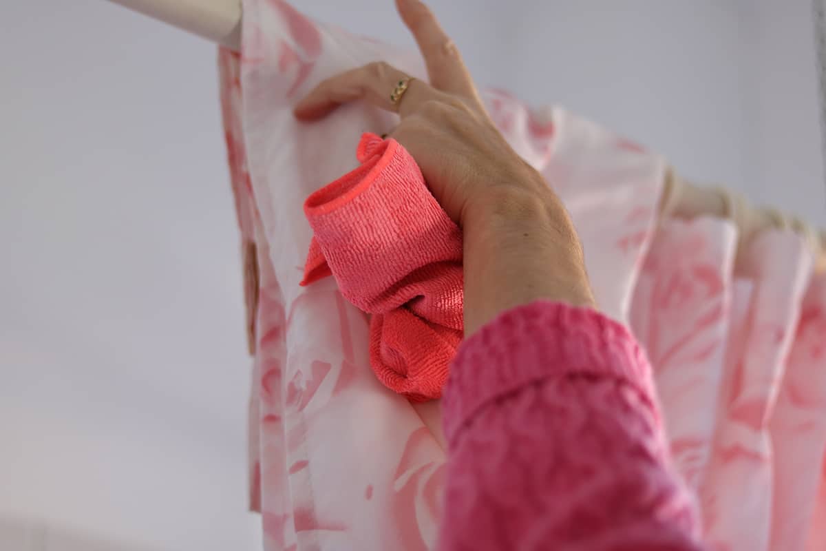 Woman cleaning bathtub curtain using rag cloth and soap spray