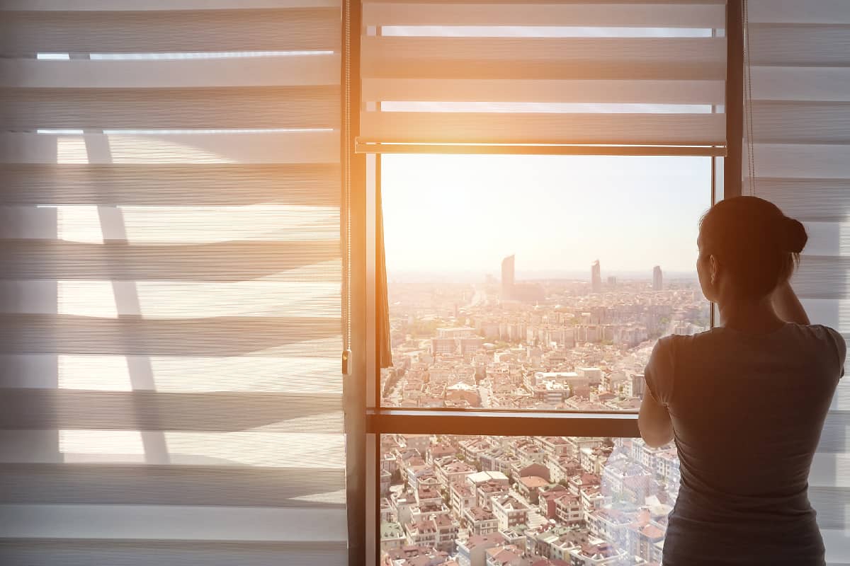 Woman is opening blinds in the morning in her modern apartment