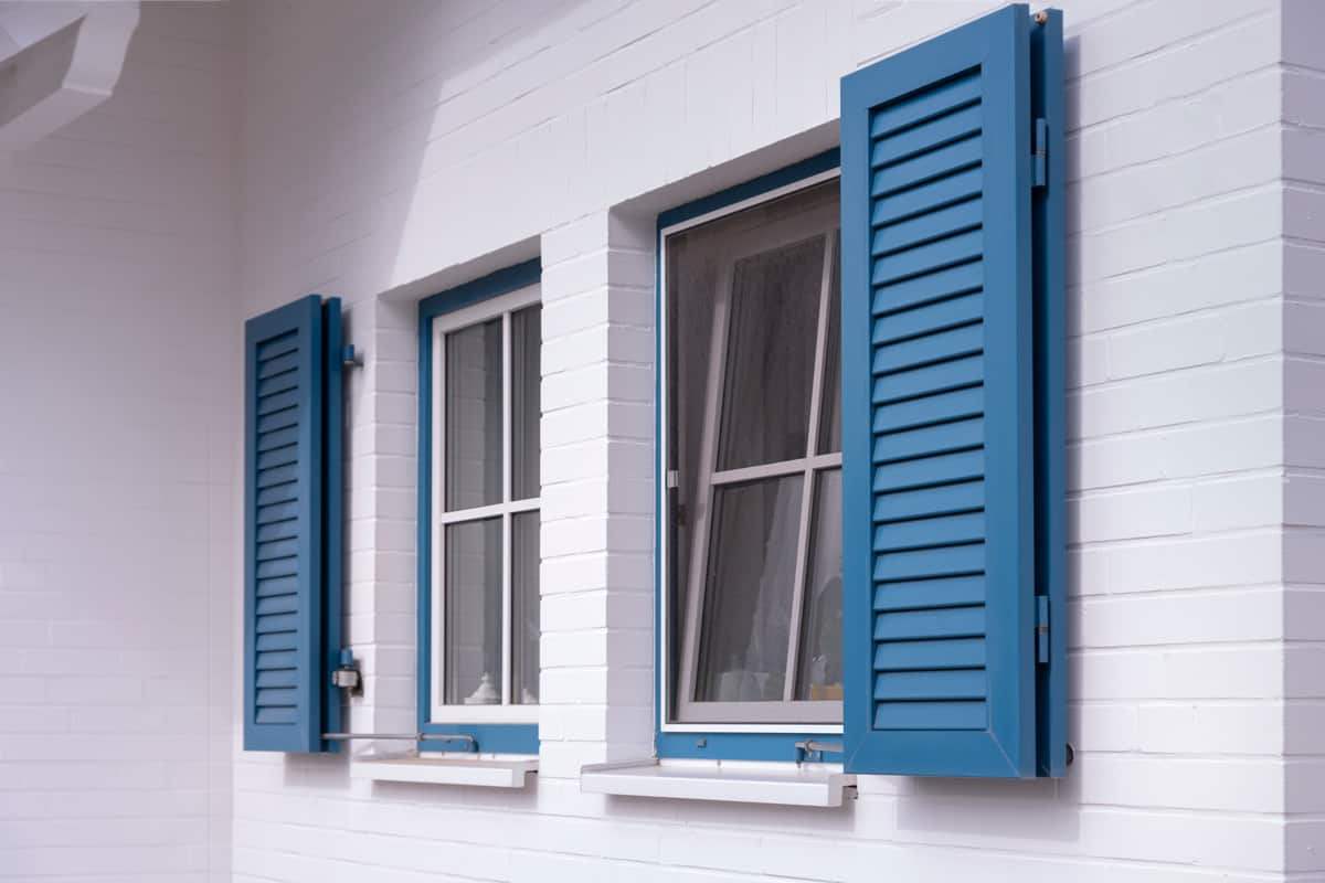 Blue louvered window shutters on a white house.