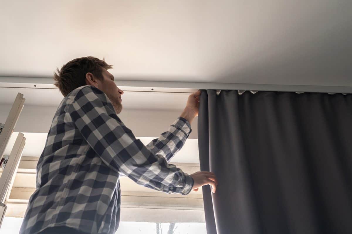 man doing house works, attach the railing and hang curtains at home


