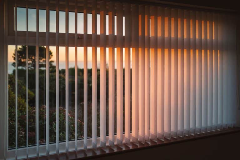 sun lit sun set photo of a wide window and a half open vertical blinds, Can You Buy Vertical Blinds Individually? [And How To Measure Your Slats For Replacement]