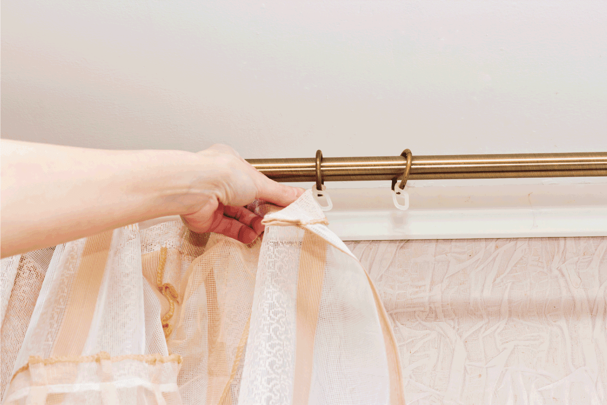 woman hangs the curtain on the hooks that are on the curtain rail.