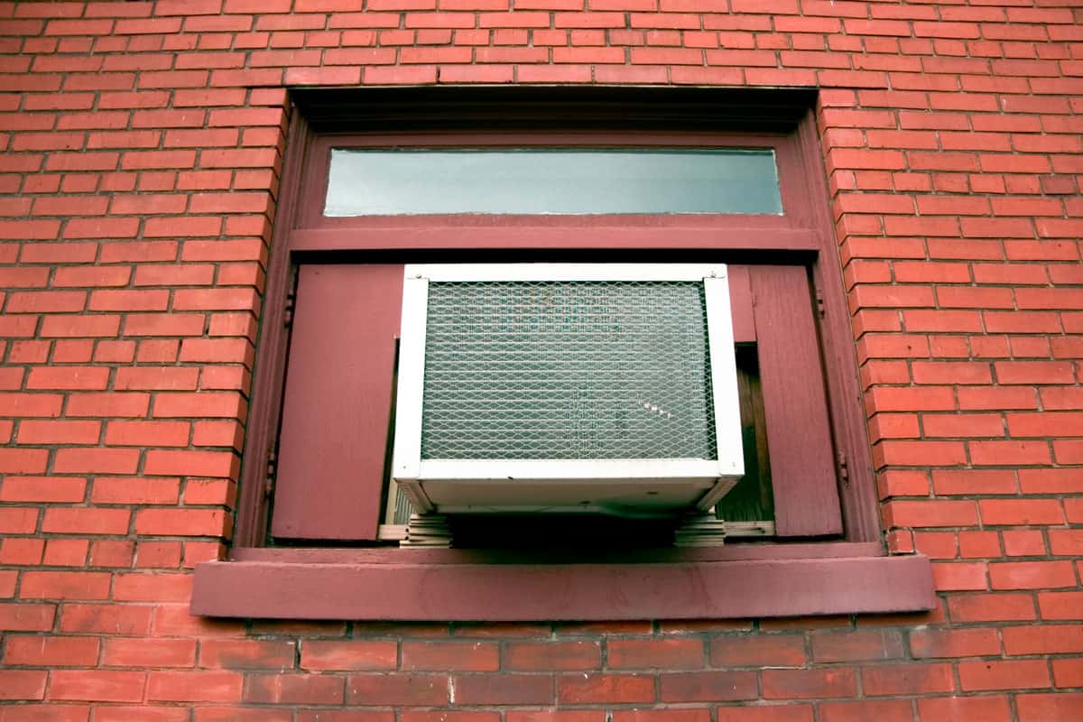 A small air conditioner in the window of a brick apartment building