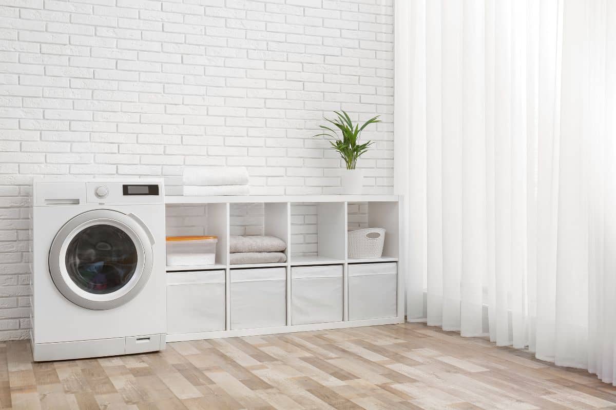 Modern washing machine near brick wall in laundry room interior, space for text
