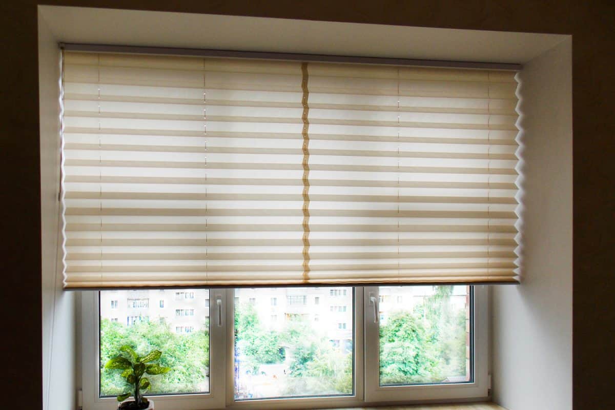 Pleated blinds XL, beige color, with 50mm fold closeup in the window opening in the interior. Home blinds - modern bottom up privacy shades half raised on apartment windows.

