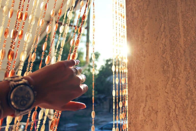 Woman moves a beaded curtain aside to see the sunlight, 17 Fabulous Indoor Beaded Curtains For Windows